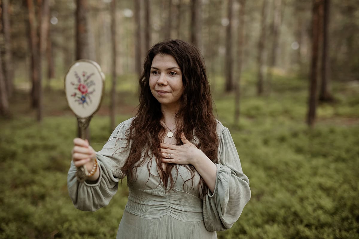 Nainen seisoo metsässä ja katsoo peiliin.