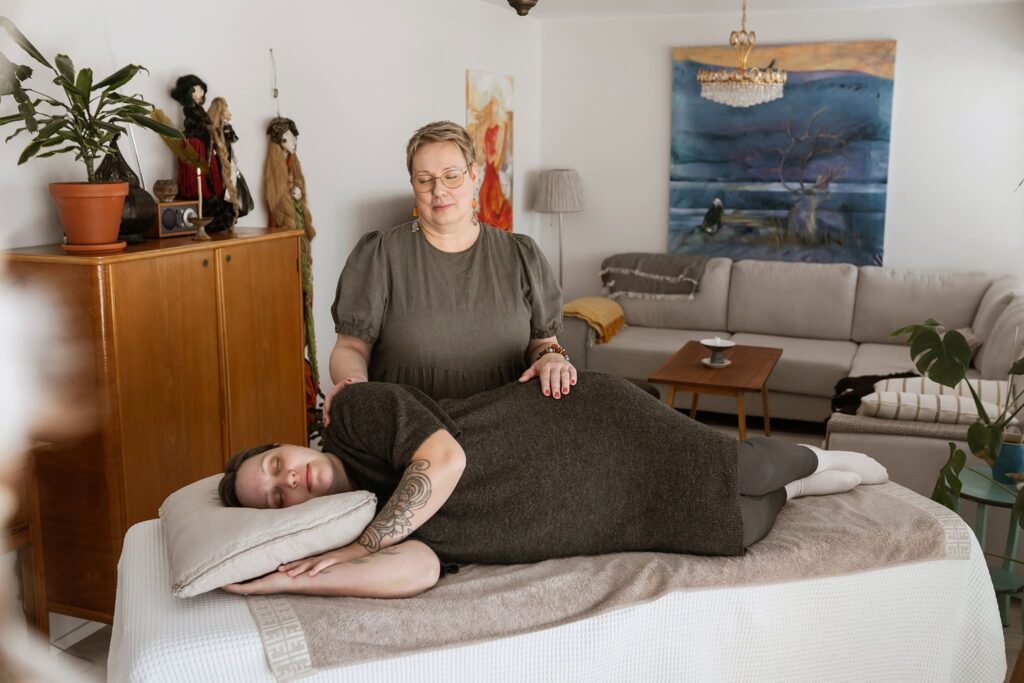 Raskaana oleva makaa ja saa reiki energiahoitoa, molemmilla silmät kiinni.