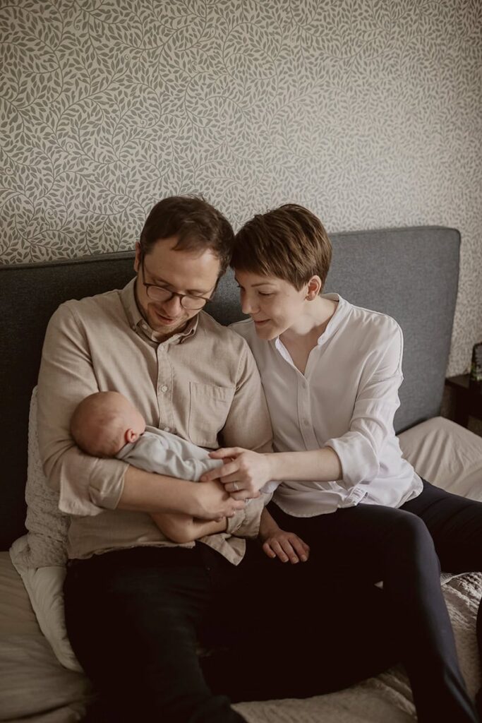 Vanhemmat istuvat sängyssä ja katsovat vastasyntynytta vauvaa.