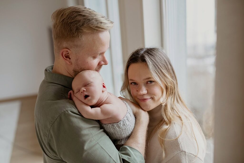 Isä pitää vauvansa sylissä kun äiti halaa heitä.